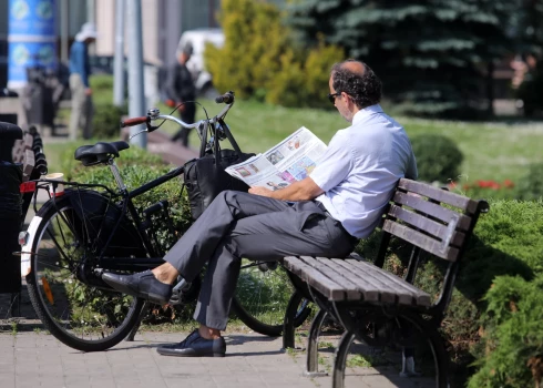 Vīrietis lasa avīzi parkā uz soliņa.