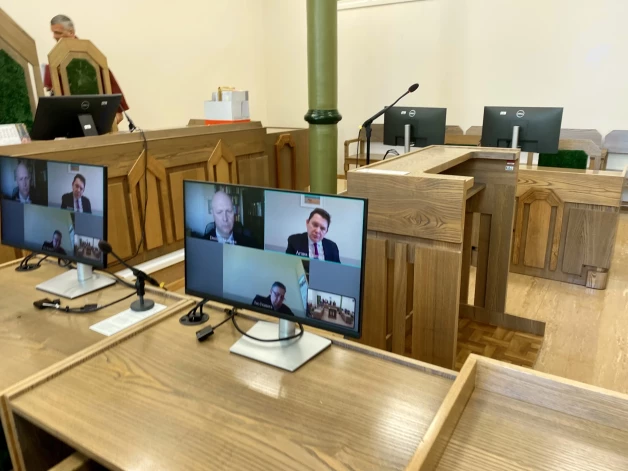 Izmantojot mūsdienu iespējas, mērot ceļu uz Kurzemes apgabaltiesu Liepājā rīdziniekiem vairs nav nepieciešams, jo sēde norit attālināti, tiesnešiem esot visā savā godībā zālē, bet apsūdzētajam Kaimiņam, prokuroram Ivo Ivanovam un advokātam Dmitrijam Skačkovam – datora ekrānā.