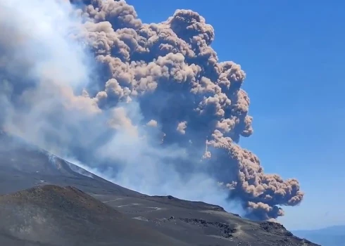 Virs Etna vulkāna redzams milzīgs dūmu un pelnu mākonis, kas paceļas skaidrās, zilās debesīs.