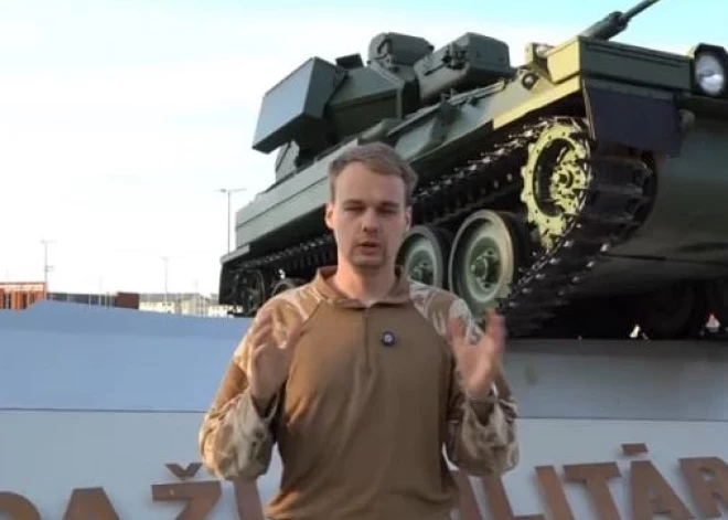 Мужчина в камуфляже на фоне военной базы в Адажи предлагает молодежи избежать службы в армии