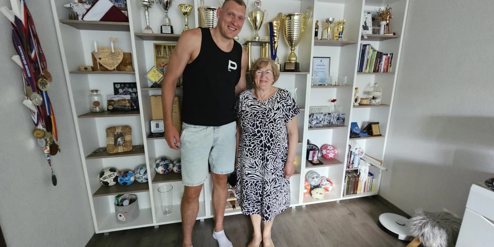 Dainis Krištopāns ar māti Regīnu, fonā pilni plaukti ar sportista trofejām.