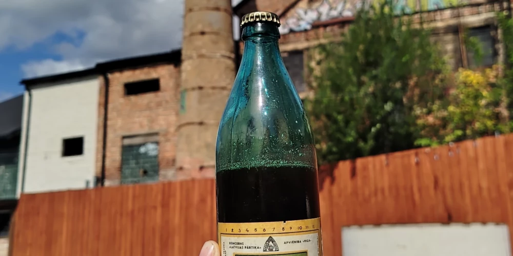Unikālā 1970. gada ražotā Rīgas miestiņa pudele (fonā – pamestās Rīgas alus fabrikas skurstenis Bruņinieku ielā (padomju okupācijas laikā - Sarkanarmijas iela).