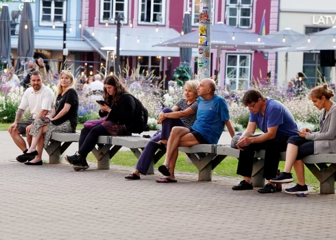 Cilvēki uz soliņa Līvu laukumā.