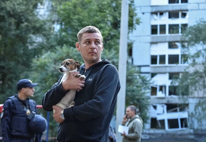 Vīrietis tur rokās savu suni, stāvot pie dzīvojamās ēkas, kas bojāta Krievijas raķešu trieciena laikā Dnipro.