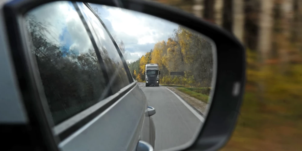 Kravas automašīna atpakaļskata spogulī, braucot pa šoseju.
