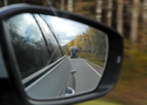 Kravas automašīna atpakaļskata spogulī, braucot pa šoseju.