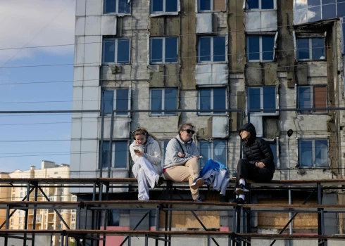 Meitenes sēž pie karā sabojātas ēkas Kijivā 2025. gada 12. oktobrī.