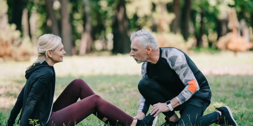 handsome mature man touching leg of injured sportswoman sitting on lawn in park