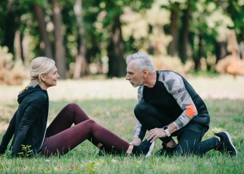 handsome mature man touching leg of injured sportswoman sitting on lawn in park