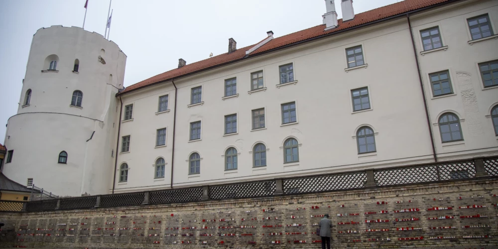 Cilvēki noliek svecītes pie Rīgas pils mūra par godu Lāčplēša dienai.