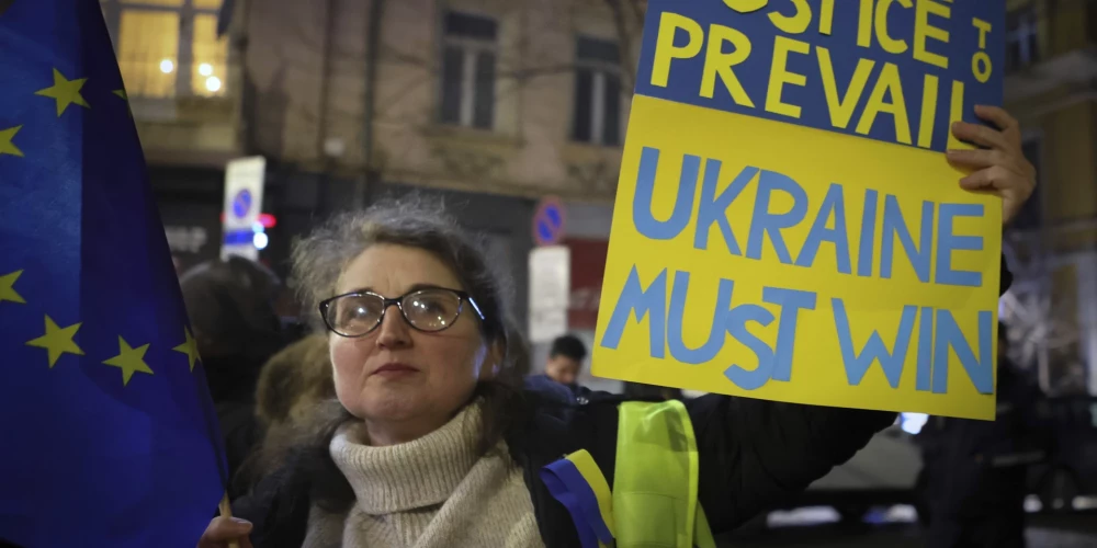 Sieviete tur plakātu ar uzrakstu "Ukrainai ir jāuzvar".