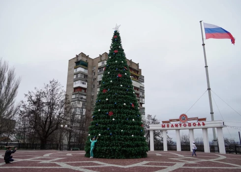 2022. gada 18. decembrī uzņemtā foto redzama sieviete, kura Melitopolē, Zaporožjes apgabalā, Ukrainā notiekošo Krievijas militāro operāciju laikā pozē fotogrāfijai ar vējā plīvojošu Krievijas karogu fonā. 