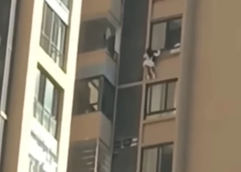 Sieviete stāv uz apmales aiz desmitā stāva loga (ekrānuzņēmums no video)