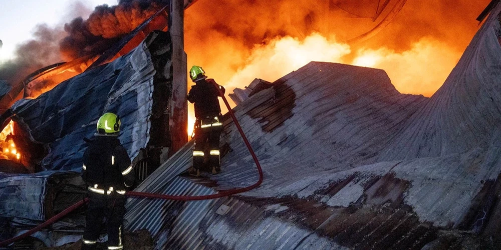 Ugunsdzēsēji Odesā dzēš liesmas sadzīves tehnikas noliktavā, kam naktī uzbrucis Krievijas bezpilota lidaparāts. 2025. gada 16. decembris.