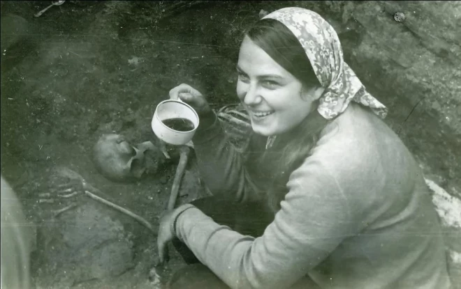 Topošā vēsturniece Dace Tabūne arheoloģijas prakses laikā Cēsu viduslaiku pilī ar kafijas krūzīti pie atsegtā sievietes skeleta, pie kura kopā ar citām senlietām bija arī septiņi ar pusi ungāru zelta dukāti. 1974. gads.