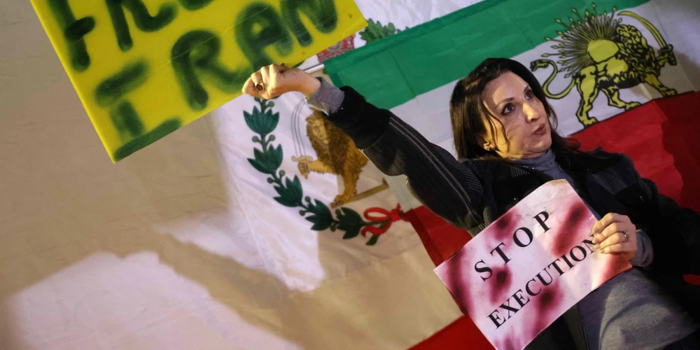 Женщина держит плакат, стоя на фоне иранского флага, использовавшегося до Исламской революции 1979 года, во время демонстрации в поддержку иранских протестующих в центральном израильском городе Холон 24 января 2026 года.