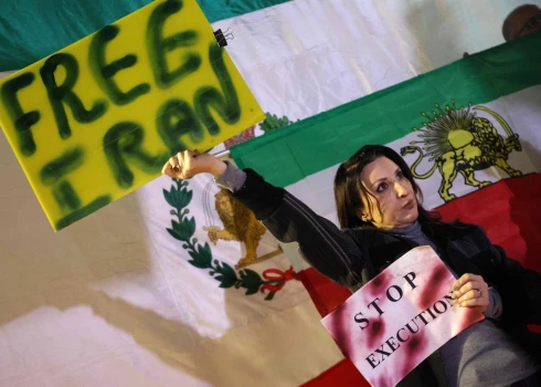 Женщина держит плакат, стоя на фоне иранского флага, использовавшегося до Исламской революции 1979 года, во время демонстрации в поддержку иранских протестующих в центральном израильском городе Холон 24 января 2026 года.