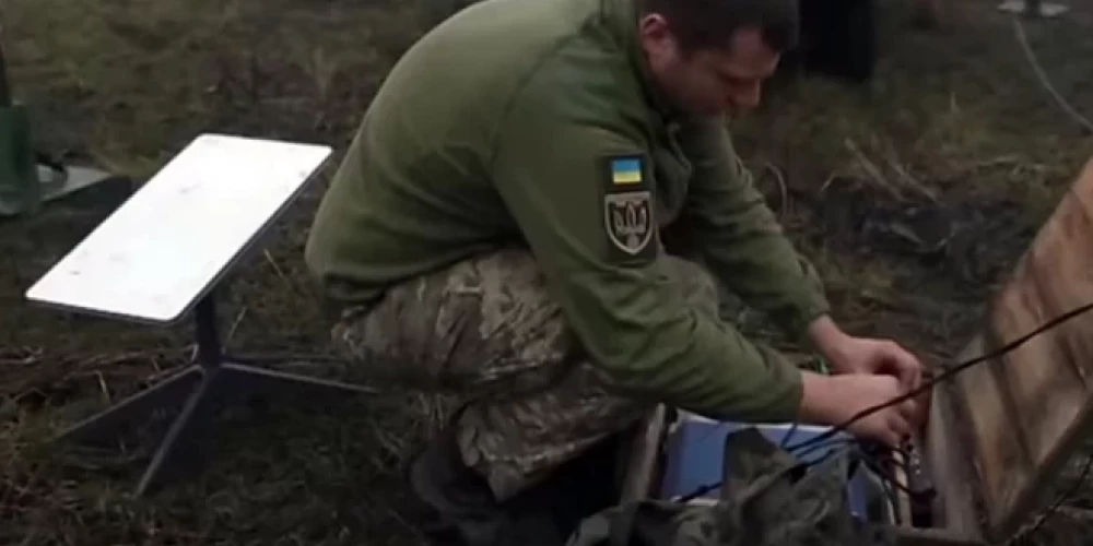 Ukraiņu karavīrs frontē uzstāda "Starlink" sistēmu.