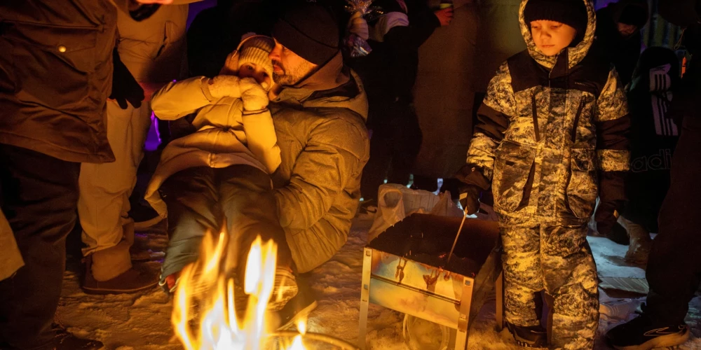 Люди греются у костра на спортивной площадке в районе, оставшемся без электричества после недавних российских ударов по гражданской инфраструктуре столицы Украины.