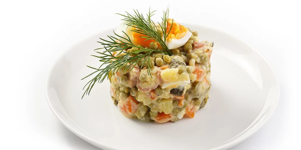 traditional east european dish for New Year's Eve - salad "Olivier" with potatoes, carrots, onion, peas, sausage, cucumbers, eggs and mayonnaise on a white plate