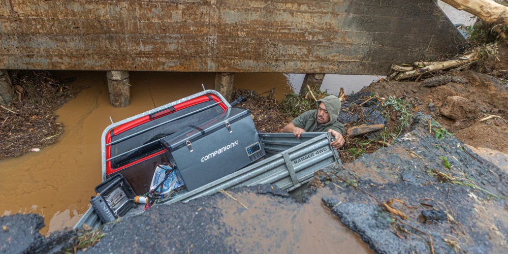 Мужчина достает вещи из служебного автомобиля, который сорвался с дороги после обрушения участка трассы из-за сильных дождей и штормового ветра в Пукетотара.