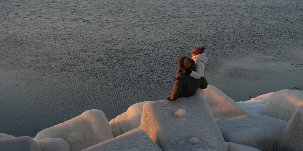 Cilvēki vēro saulrietu uz Mangaļsalas mola.