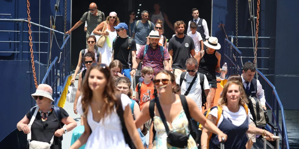 Tūristi izkāpj no laivas Santorini ostā. 