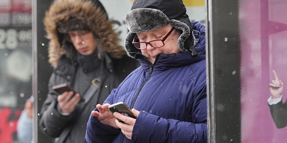 Sanktpēterburgas iedzīvotāji autobusu pieturā vēro savus mobilos telefonus.