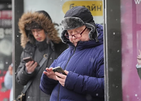 Sanktpēterburgas iedzīvotāji autobusu pieturā vēro savus mobilos telefonus.