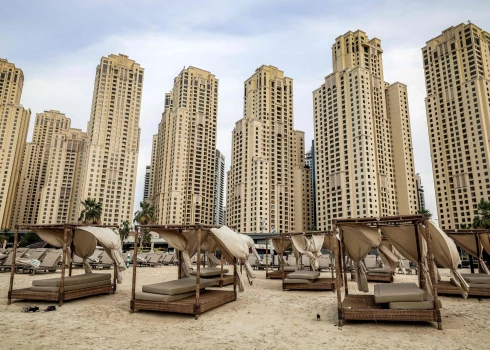 Пустые шезлонги стоят на пляже на фоне высотных зданий района Jumeirah Beach Residence в Дубае в середине марта 2026 года.