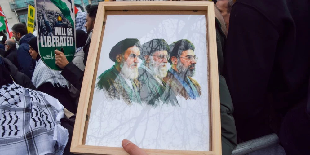 Palestīniešu un islāmistu Irānas piekritēju demonstrācijā Londonā protestētājs tur plakātu, kur attēloti visi trīs Irānas augstākie vadoņi - no kreisās: Ruholla Homeini (1979-1989), Ali Hameneji (1989-2026) un Modžtaba Hameneji (2026).