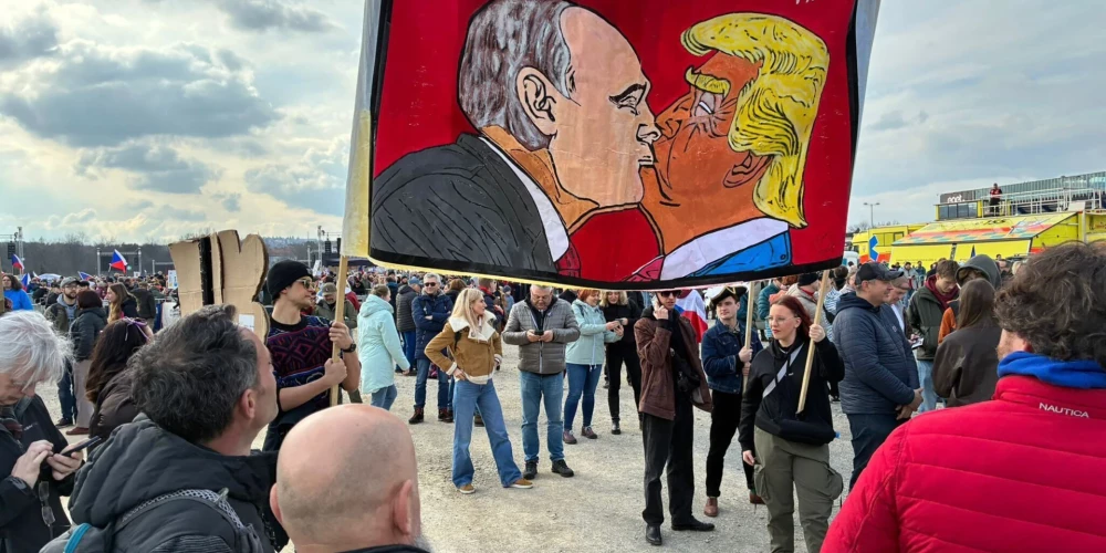 Protestētāji Prāgas ielās tur plakātu ar stilizētu Donalda Trampa un Vladimira Putina skūpstu.