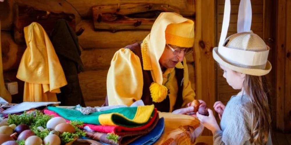 Lieldienu noskaņās Tērvetes rūķis dzeltenā cepurē ar lielu pušķi galā pēta krāsoto olu kopā ar mazu meiteni, kurai galvā cepure ar pielīmētām zaķa ausīm.