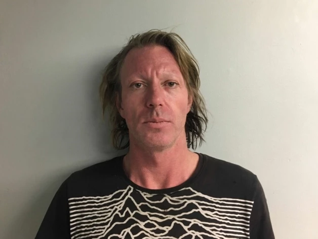 Elijas Blū Olmena foto, kas uzņemts pēc aresta policijas iecirknī 2026. gada februārī.