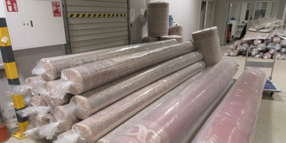 Vairāki grīdas paklāji plastmasas iepakojumos.