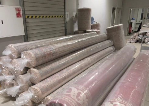 Vairāki grīdas paklāji plastmasas iepakojumos.