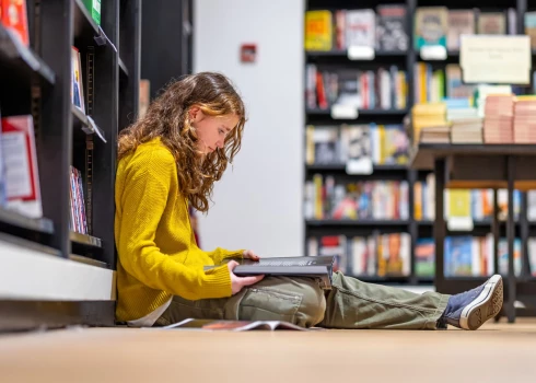 Meitene aizrautīgi lasa bibliotēkā (foto: Shutterstock)