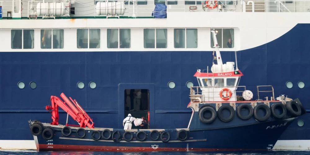 Человек в костюме химзащиты передает посылку на круизный лайнер MV Hondius в порту Гранадилья-де-Абона.