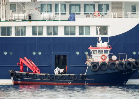 Человек в костюме химзащиты передает посылку на круизный лайнер MV Hondius в порту Гранадилья-де-Абона.