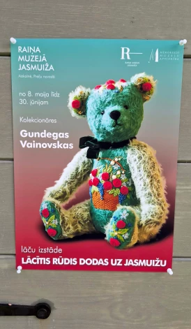 Uz izstādes afišas redzams Gundegas O. Vainovskas pašas roku darinātais un izšūtais lācītis Ofēlija.
