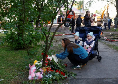 Женщина с детьми возлагает цветы к стихийному мемориалу на месте жилого дома.