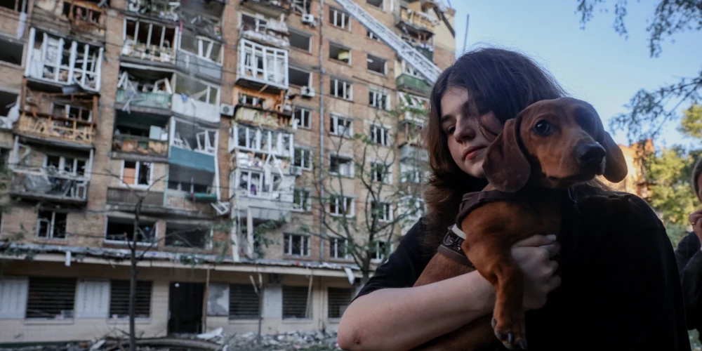 Жительница с собакой стоит у поврежденного жилого дома после ночного российского ракетно-дронового удара по Киеву. 
