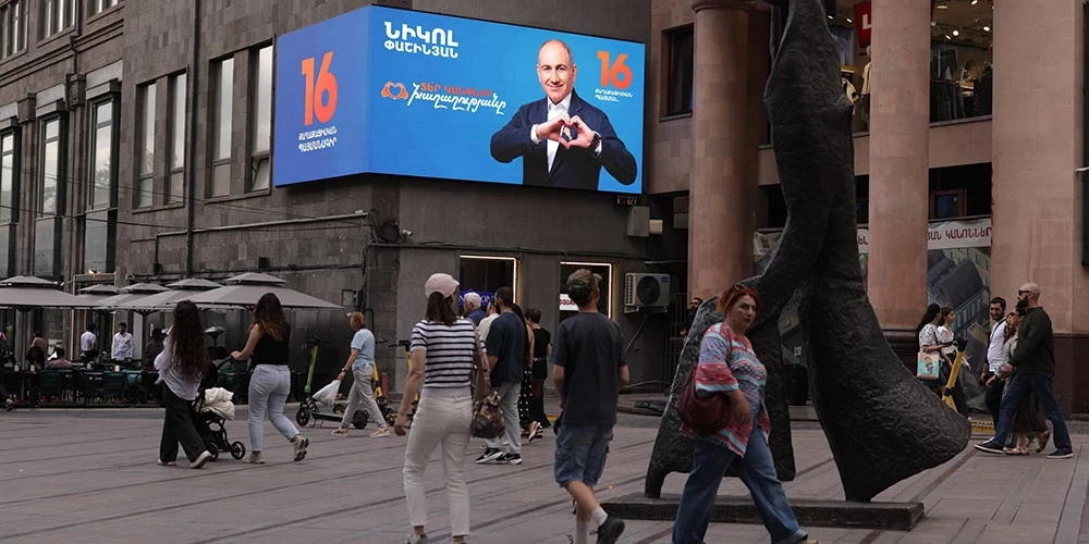 Cilvēki pastaigājas pa ielu Erevānā netālu no Armēnijas premjerministra Nikola Pašinjana kampaņas reklāmas.