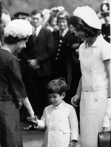 Karaliene Elizabete II sasveicinās ar Džonu F. Kenediju junioru un viņa mammu Žaklīnu Kenediju 1965. gadā.